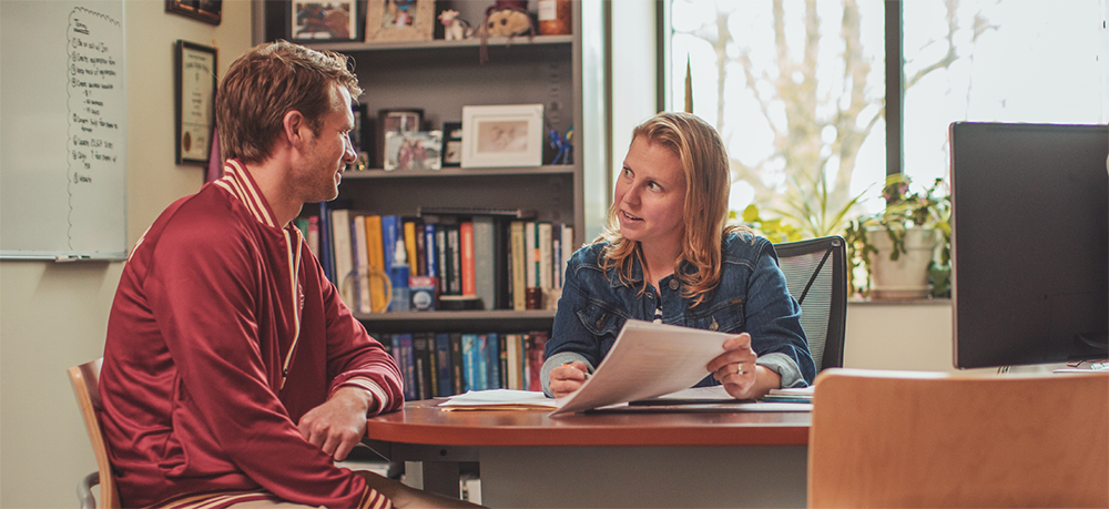 Image of a professor helping a student with work at a table